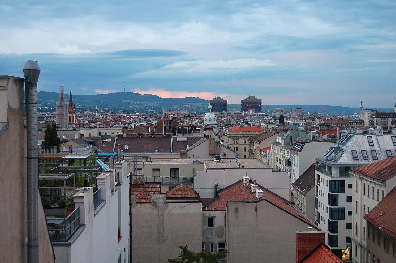 View from the spire of St. Laurenz am Schottenfeld church over Neubau district towards north. Visible are the spires of Altlerchenfeld church (left), the towers of Allgemeines Krankenhaus (General hospital – centre), and the smokestack of Spittelau garbage processing plant; in the background Kahlenberg, Leopoldsberg, and Bisamberg mountains.